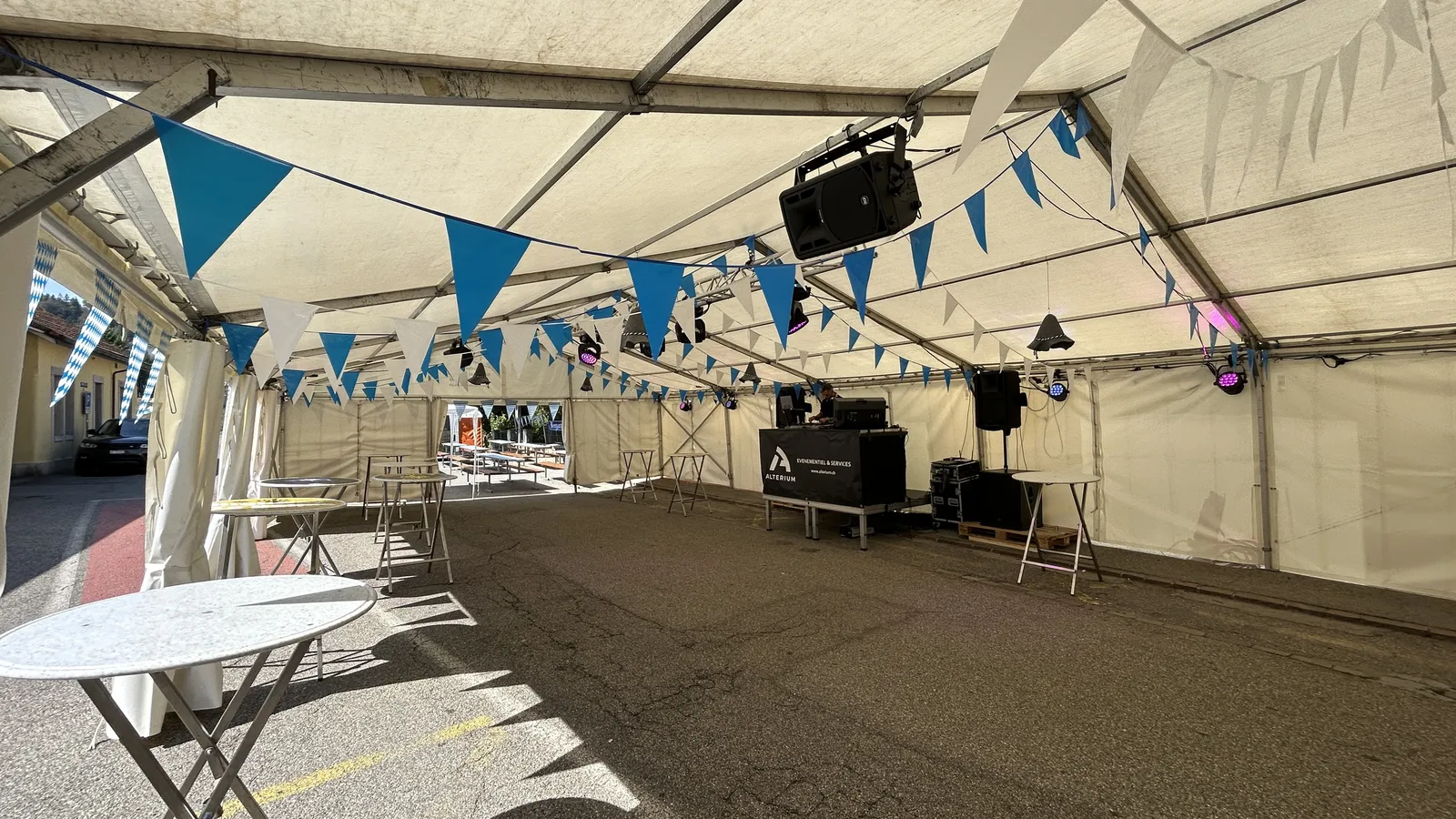 Tente de Montoz & Co. décorée de fanions bleus et blancs, avec la régie DJ Alterium, une enceinte suspendue et des projecteurs LED fixés à la charpente