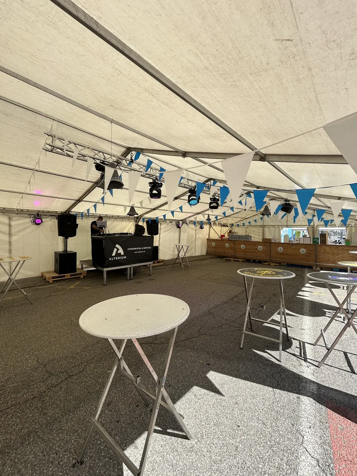 Structure en truss équipée de lyres au-dessus de la régie DJ Alterium posée sur des praticables, sous la tente