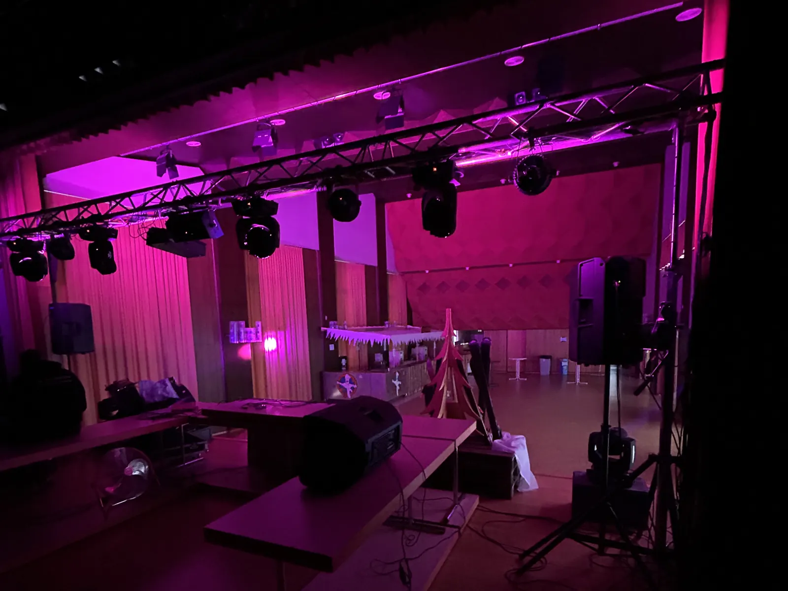 Salle de Péry avant la soirée après-ski : lyres sur une structure truss devant la scène, enceinte sur pied et poste DJ, sous un éclairage rose, lors de l'édition 2025