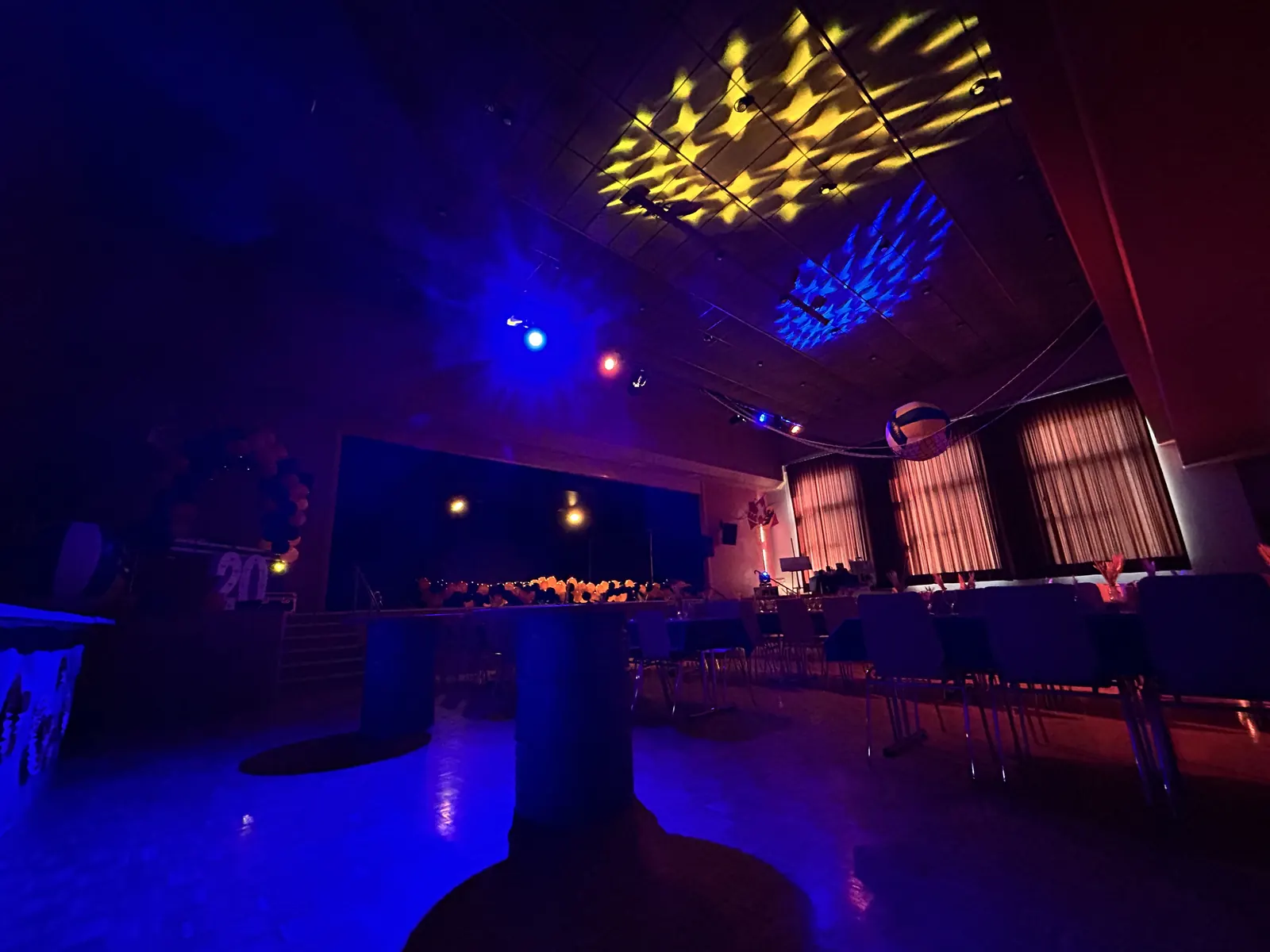 Gobos jaunes et bleus projetés au plafond de la salle, au-dessus des tables et de la scène, dans une ambiance bleue